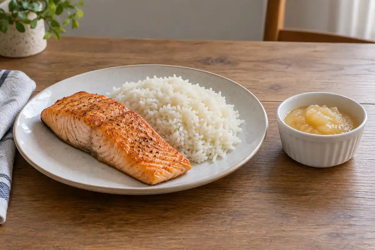 Assiette de saumon grillé et de riz blanc, avec un ramequin de compote de pommes posé à côté.